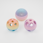 Three PawQuest prey balls from production V14: Ringed treat-opening ball in Paint Splash at left, Mosaic treat-opening ball in Dreamy Dusk at right, and ventilated Mesh ball in Vibrant Coral behind. Multicolour PLA; colour transitions vary by print. No glow filament.